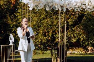 un' femmina maestro di cerimonie è vestito nel un' bianca completo da uomo, durante un' discorso. foto