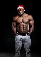 contento nuovo anno. pieno lunghezza Visualizza di il sexy muscolare uomo indossare Natale cappello in piedi pensieroso con nudo torso. nudo bodybuilder in posa per telecamera a studio foto