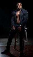 pieno lunghezza Visualizza di il africano americano bodybuilder in piedi con fiducia su nero studio sfondo. uomo dimostrando il suo stampa e muscoli foto