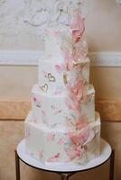 un' grande lussuoso multilivello nozze torta è decorato con fresco rosa zucchero fiori nel il banchetto sala. nozze dolce sotto il sera luce. nozze arredamento. foto
