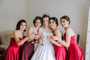 foto con damigelle d'onore potabile Champagne a partire dal bicchieri nel il mattina nel un' bellissimo Hotel. foto di un' bellissimo giovane sposa e sua amici nel accoppiamento vestiti potabile Champagne prima il nozze.