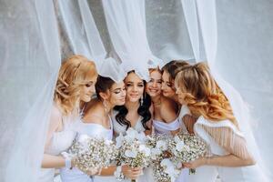 nozze fotografia nel natura. un' brunetta sposa e sua amiche posa sotto un' velo, Tenere mazzi di fiori foto