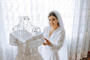 sposa toccante sua nozze vestire. alto qualità foto. un' bellissimo giovane sposa nel un' bianca sottoveste è in piedi di il letto, toccante sua nozze vestire. foto