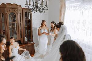 damigelle d'onore rallegrarsi nel il mattina, porzione per allacciare il pulsanti su il nozze vestito e preparare per il nozze cerimonia. essi prendere immagini, Sorridi, Aiuto il sposa con sua scarpe. foto