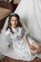 ritratto di un incredibilmente bellissimo ragazza sposa nel un' bianca accappatoio nel il Camera da letto, il sposa pose nel il mattina prima il nozze cerimonia. foto