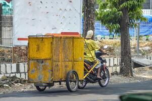 un' spazzino chi tira un' giallo spazzatura carrello utilizzando un' moto, Indonesia, 2 novembre 2023. foto