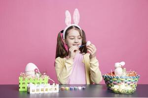 piccolo allegro bambino piccolo decorazione uova con acquerello per Pasqua vacanza preparativi, colorazione festivo ornamenti contro rosa sfondo. giovane poco ragazza avendo divertimento con arte e mestiere. foto