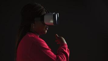 vista laterale di creativo giovane femmina godendo simulazione con interattivo tecnologia indossare 3d virtuale la realtà occhiali. africano americano fashionista utilizzando un' sofisticato vr cuffia. foto