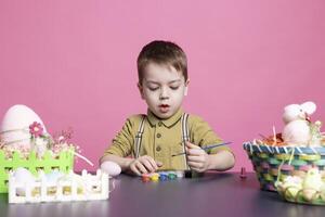 gioioso piccolo bambino decorazione uova e ornamenti con acquerello, colorazione e lavorazione decorazioni nel tempo per Pasqua Domenica celebrazione. giovane allegro ragazzo pittura con cravatta tintura. foto