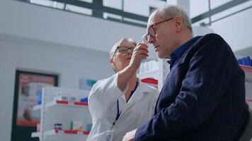 anziano farmacista nel farmacia utilizzando elettronico termometro su anziano uomo, controllo temperatura. vecchio paziente e assistenza sanitaria specialista durante annuale visita medica, monitoraggio influenza sintomi come come febbre foto