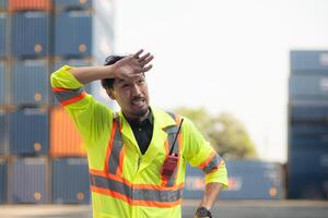 ritratto di un asiatico maschio lavoratore indossare un' sicurezza veste e difficile cappello, assunzione un' rompere a partire dal opera con un' contenitore scatola nel il sfondo foto