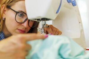 donna sarta nel bicchieri lavori su macchina da cucire a sua posto di lavoro nel laboratorio foto