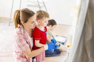 madre con sua bambini pittura il parete con dipingere utilizzando rullo e spazzola foto