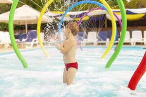 un' bambino sta sotto Fontana avendo divertimento con acqua spruzzi nel il piscina foto