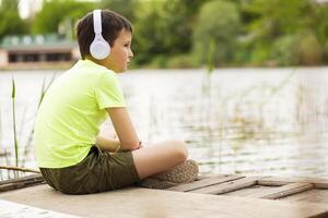 un' ragazzo con cuffie ascoltando per musica a in riva al lago foto