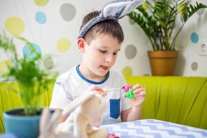 contento Pasqua. ragazzo nel coniglietto orecchie coloranti colorato uovo per Pasqua caccia foto