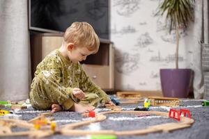 bambino giocando con giocattolo Ferrovia, treni e macchine su il pavimento foto