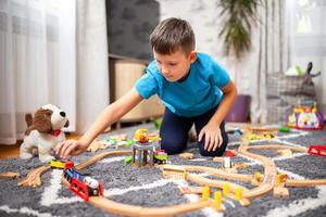 ragazzo giocando con giocattolo treno con di legno rotaie mentre seduta su pavimento a casa foto