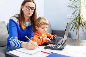 giovane donna Lavorando a casa con un' il computer portatile con un' bambino su sua giro foto