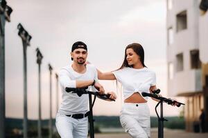 un' ragazza e un' tipo siamo a piedi su elettrico scooter in giro il città, un' coppia nel amore su scooter. foto