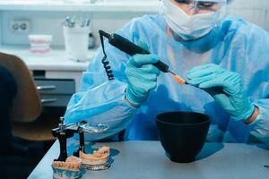 un' mascherato e guantato dentale tecnico lavori su un' protesico dente nel il suo laboratorio foto