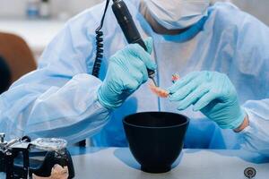 un' mascherato e guantato dentale tecnico lavori su un' protesico dente nel il suo laboratorio foto