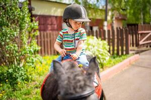 bellissimo poco ragazza Due anni vecchio equitazione pony cavallo nel grande sicurezza fantino casco in posa all'aperto su campagna foto