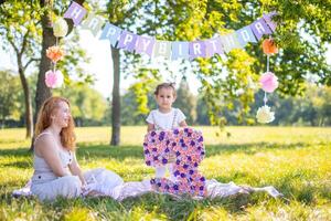 allegro madre e figlia avendo divertimento su bambino compleanno su coperta con carta decorazioni nel il parco foto