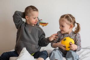 piccolo ragazzo con giù sindrome giochi con il suo minore sorella su il letto nel casa Camera da letto. alto qualità foto