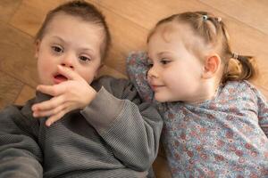 piccolo ragazzo con giù sindrome giochi con il suo minore sorella nel casa Camera da letto. alto qualità foto