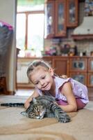 carino poco ragazza con grigio gatto dire bugie su tappeto nel casa vivente camera foto