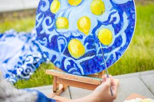 Visualizza di mano di giovane donna pittura immagine di limoni su blu coperta nel casa terrazza. alto qualità foto