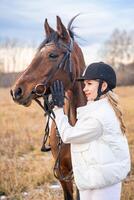 bellissimo biondo professionale femmina fantino nel casco in piedi vicino cavallo. amicizia con cavallo foto