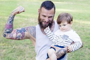 tatuato padre avere divertimento con il suo figlio nel il parco foto