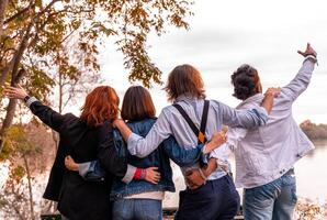 gruppo di migliore amico avere divertimento nel davanti di un' grande fiume nel autunno a tramonto foto