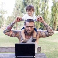 tatuato papà avere divertimento con il suo figlio e il computer portatile foto