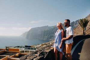 un' coppia nel amore sta su un osservazione ponte contro il fondale di il acantilados de los gigantes montagne a tramonto, tenerife, canarino isole, Spagna foto