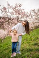 giovane donna con poco figlia nel un' fioritura rosa e bianca giardino petrin nel praga, primavera tempo nel Europa. alto qualità foto