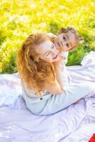 mamma e figlia ridendo e abbracciare seduta su un' coperta nel il parco il concetto di un' contento famiglia, amicizia, e amore. foto