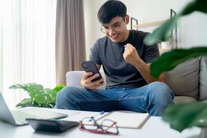 contento eccitato uomo guardare a mobile Telefono, uomo ricevente bene notizia utilizzando smartphone a casa. foto