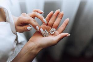 il sposa detiene nel sua mani e Spettacoli sua orecchini con prezioso pietre, avvicinamento. mattina di il sposa. il nozze giorno. foto