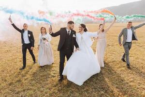 nozze foto sessione nel natura. sposa e sposo e loro amici nel un' campo, allegramente Tenere colorato Fumo.