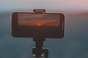 un' smartphone è registrazione il sole ambientazione al di sopra di un' montagna gamma. foto