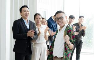 un' gruppo di persone siamo sorridente e battendo le mani, con uno uomo nel un' floreale camicia in piedi fuori. scena è contento e celebrativo foto