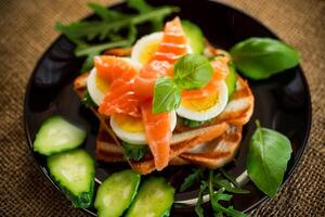 cucinato Sandwich con leggermente salato rosso pesce, cetrioli e bollito uova con erbe aromatiche. foto