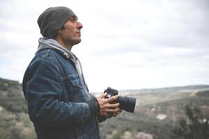 giovane uomo, viaggio fotografo Tenere professionale digitale telecamera, cattura bellissimo Visualizza mentre escursioni a piedi nel montagne foto