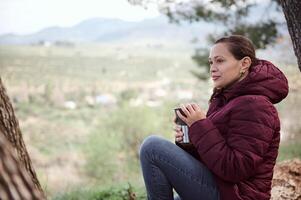 bellissimo latino americano giovane donna turista, viaggiatore avventuriero rilassante nel il foresta, con un' thermos boccale nel mani foto