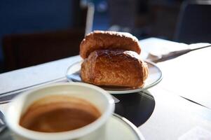 un' prima colazione nel francese tradizioni. Due appena al forno croccante Cornetti e tazza di caffè su il tavolo nel un' marciapiede bar. foto
