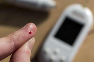 donna pungere sua dito per dai un'occhiata sangue glucosio livello con glucometro, test sangue glucosio per diabete foto