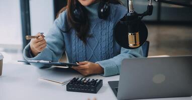 donna registrazione un' Podcast su sua il computer portatile computer con cuffie e un' microscopio. femmina podcaster fabbricazione Audio Podcast a partire dal sua casa studio. foto